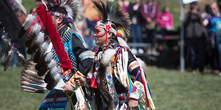 two Native Americans wearing decorative clothing for pow-wow